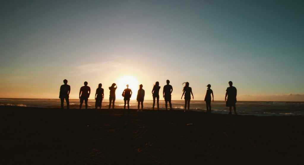 People captured from behind standing side by side, looking at the sun setting in front of them